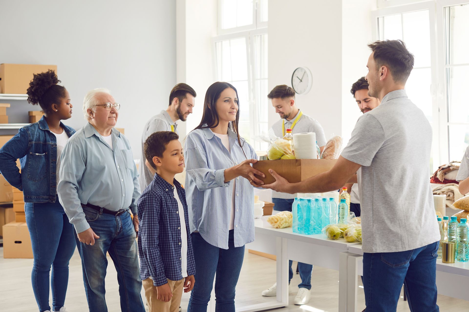 Volunteers receiving boxed food at a bright community pantry, with one person handing supplies across a table