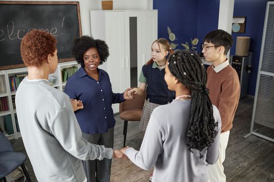 Small group talking in a classroom, standing near a chalkboard and chairs.