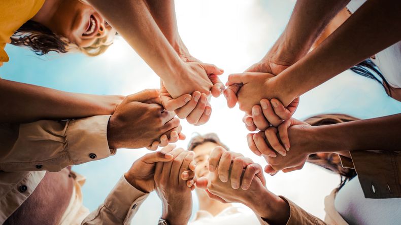 Hands stacked together in a circle against a bright sky, symbolizing teamwork and unity