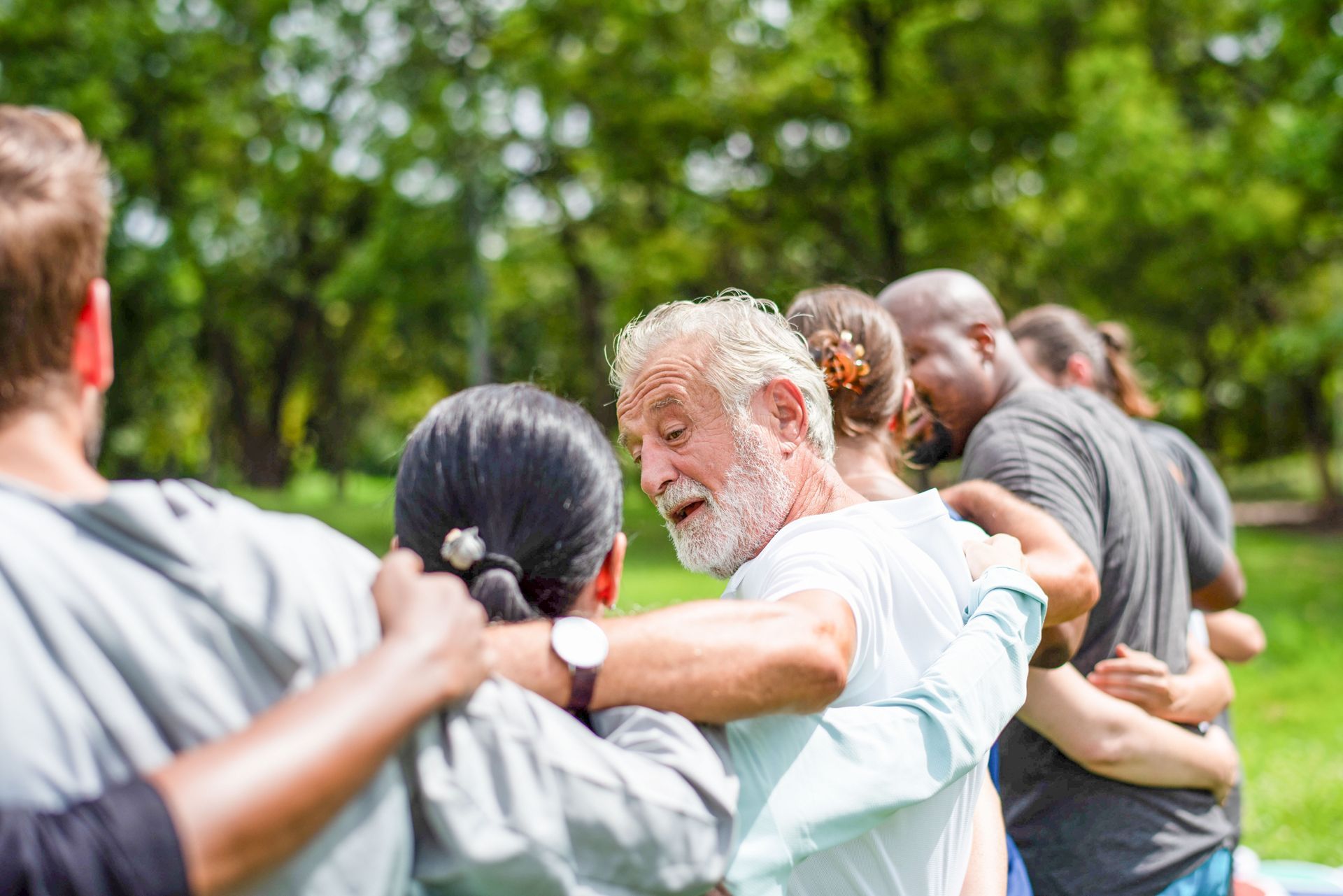 People standing in a line outdoors, holding shoulders in a group exercise or team-building activity.