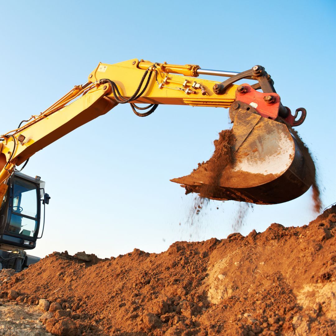 Yellow excavator digging brown soil under a blue sky.