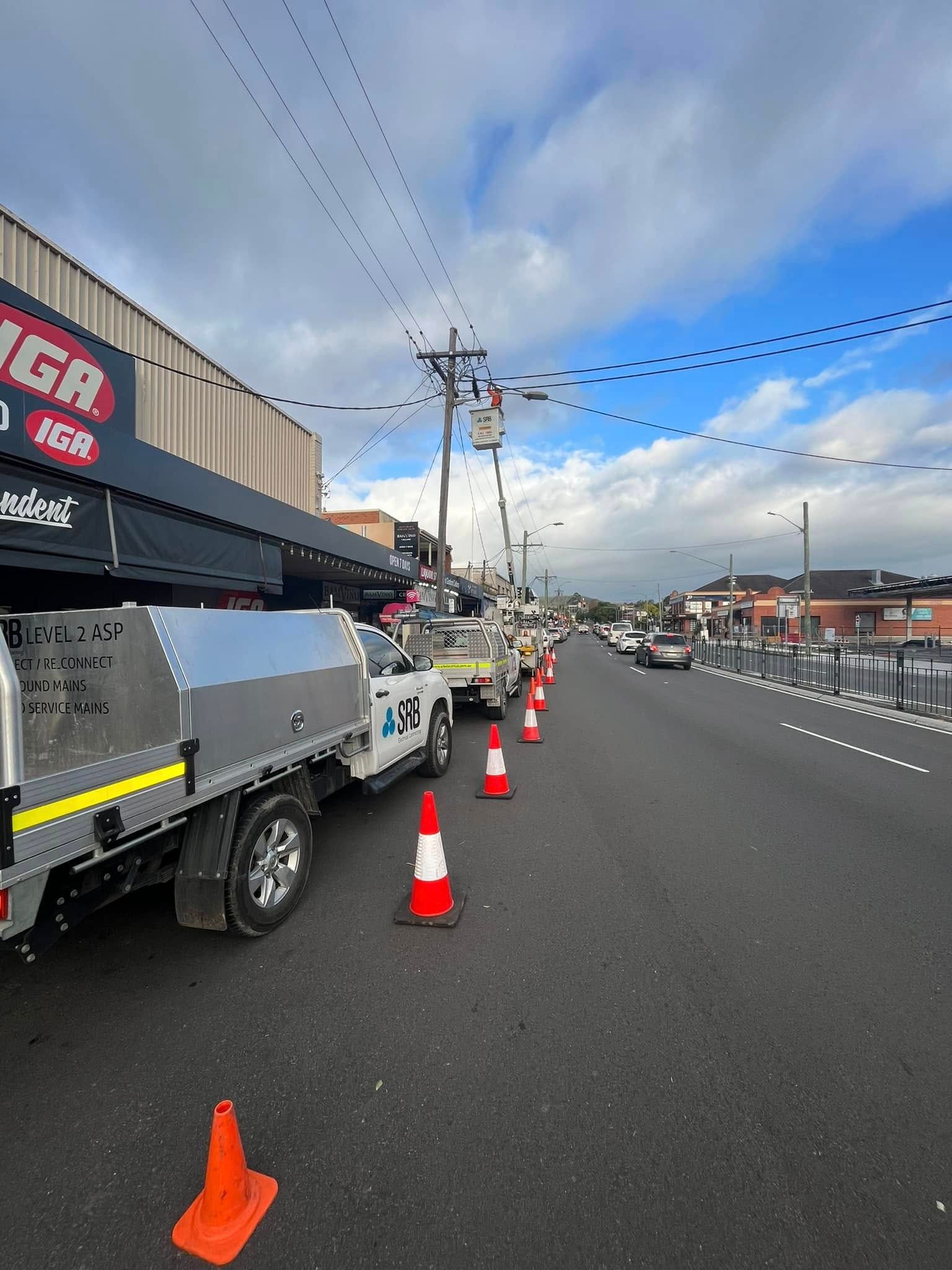 Roadside Work Zone With Parked Utility Trucks, Orange Cones, and a Wet City Street — SRB Electrical Contracting Pty Ltd In Davistown, NSW