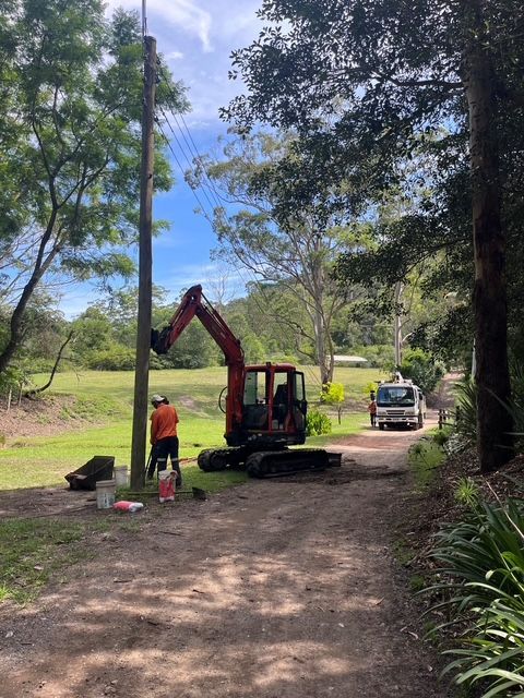 Workers operate an excavator on a dirt path in a wooded area, with a utility truck nearby. — SRB Electrical Contracting Pty Ltd In Davistown, NSW