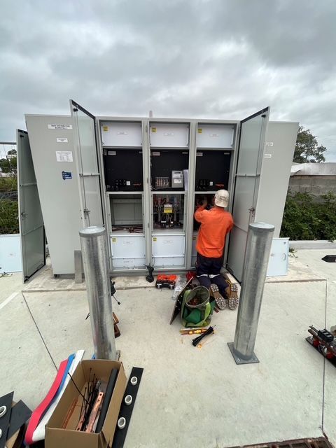 Worker in orange vest repairing rooftop electrical cabinets under a cloudy sky. — SRB Electrical Contracting Pty Ltd In Davistown, NSW