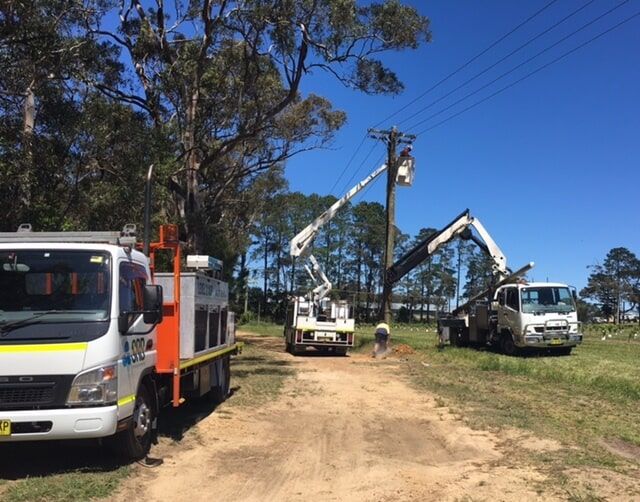 Utility trucks and tree-trimming booms lined up on a dirt road under a clear blue sky. — SRB Electrical Contracting Pty Ltd In Sydney, NSW