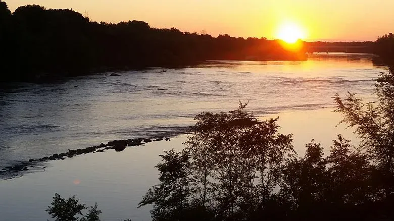 Golden sunset over a calm river surrounded by trees, with light reflecting on the water's surface.