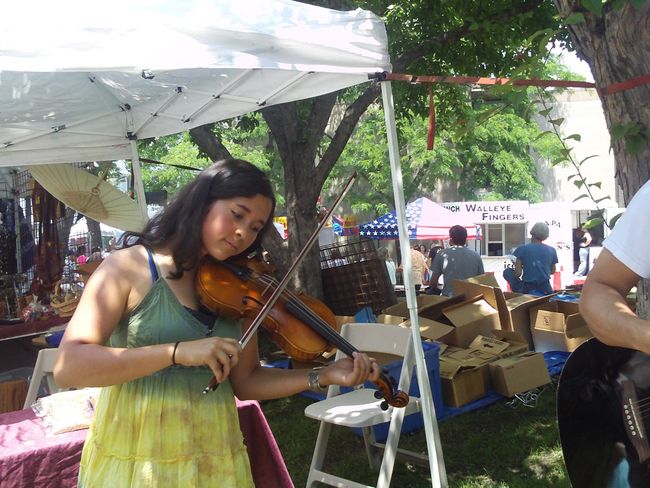 Woman playing violin under a white canopy at an outdoor market booth