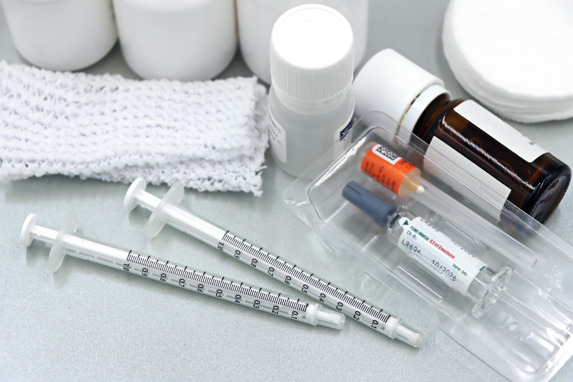 Medical supplies including two insulin syringes, vials, a small medicine bottle, and white gauze on a gray surface.