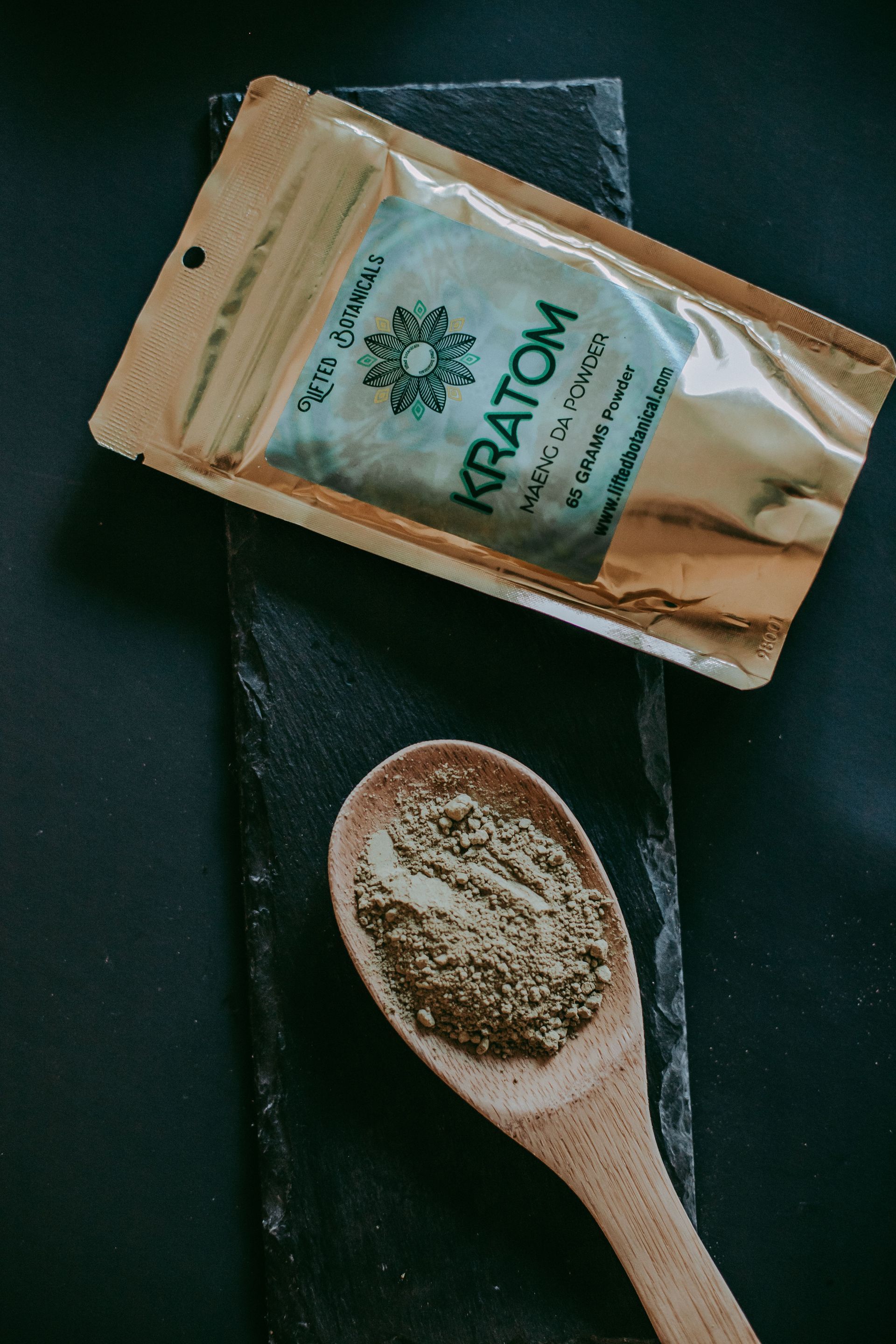 Wooden spoon with ground spice beside a small packet on a dark surface