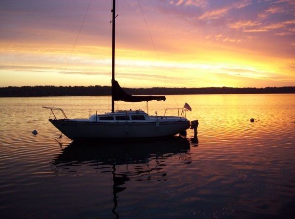 Sailboat silhouetted on calm water at sunset with orange and pink sky