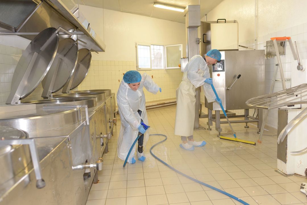 Operai con indumenti protettivi puliscono una sala di lavorazione alimentare in acciaio inossidabile con tubi e macchinari