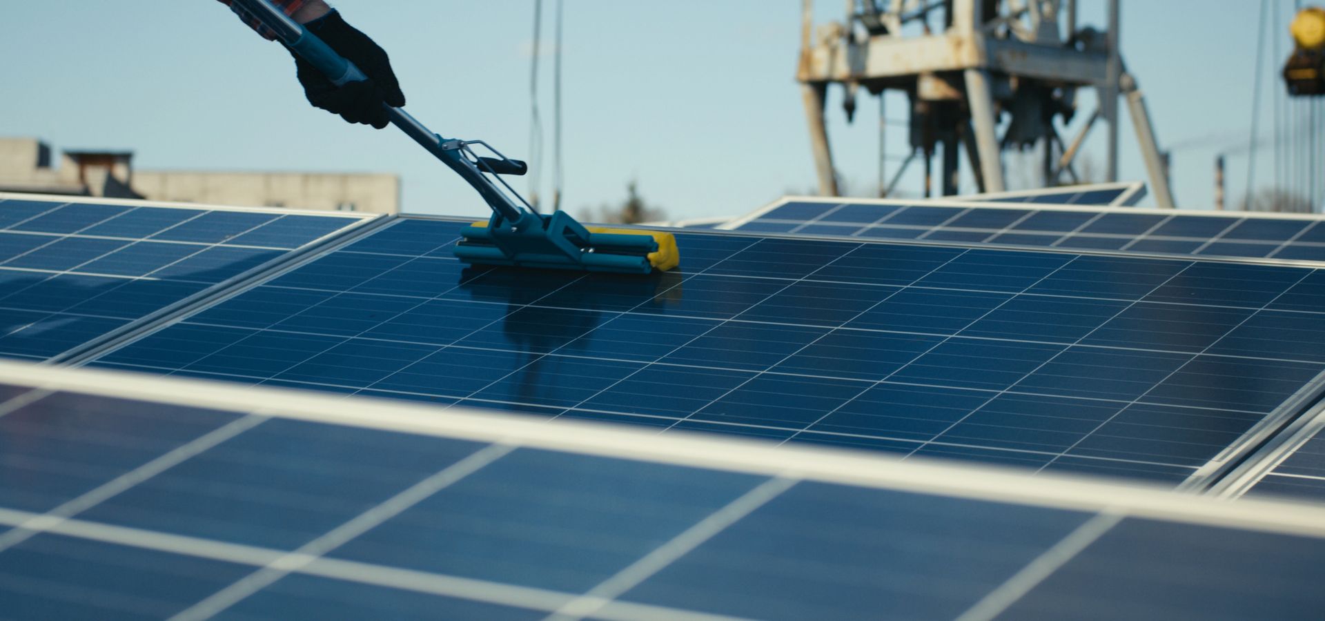 Un pannello solare viene pulito con una spazzola su un tetto, con torri industriali sullo sfondo.