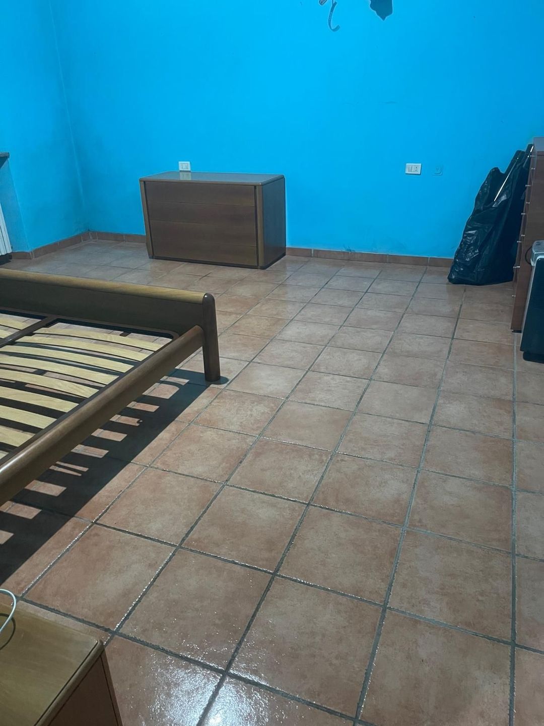 Prodotti per la pulizia ammucchiati su una superficie di legno, tra cui guanti, flaconi spray, spugna e spazzola.