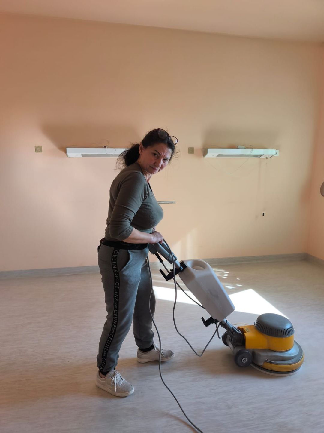 Corridoio ospedaliero con carrello per le pulizie e materiali in primo piano, persona che cammina in lontananza.
