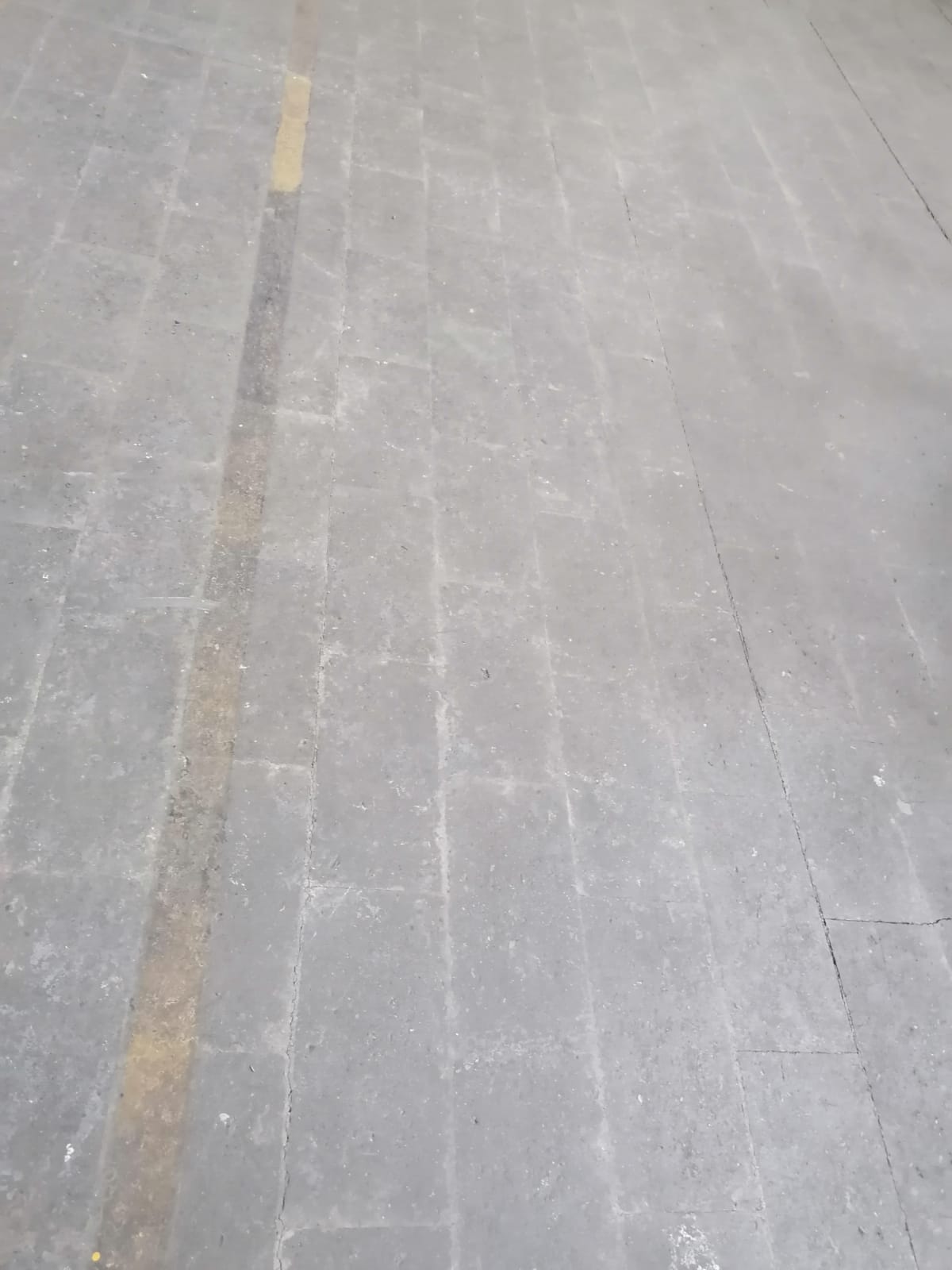 Pavimentazione piastrellata grigia con una linea gialla che corre lungo il centro.