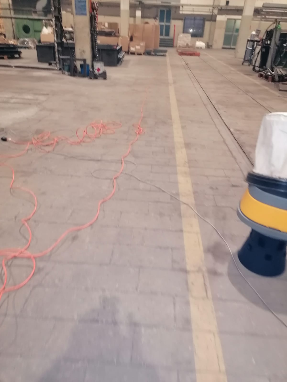 Pavimento di un magazzino industriale con prolunghe arancioni, pallet e macchinari lungo un percorso segnalato.