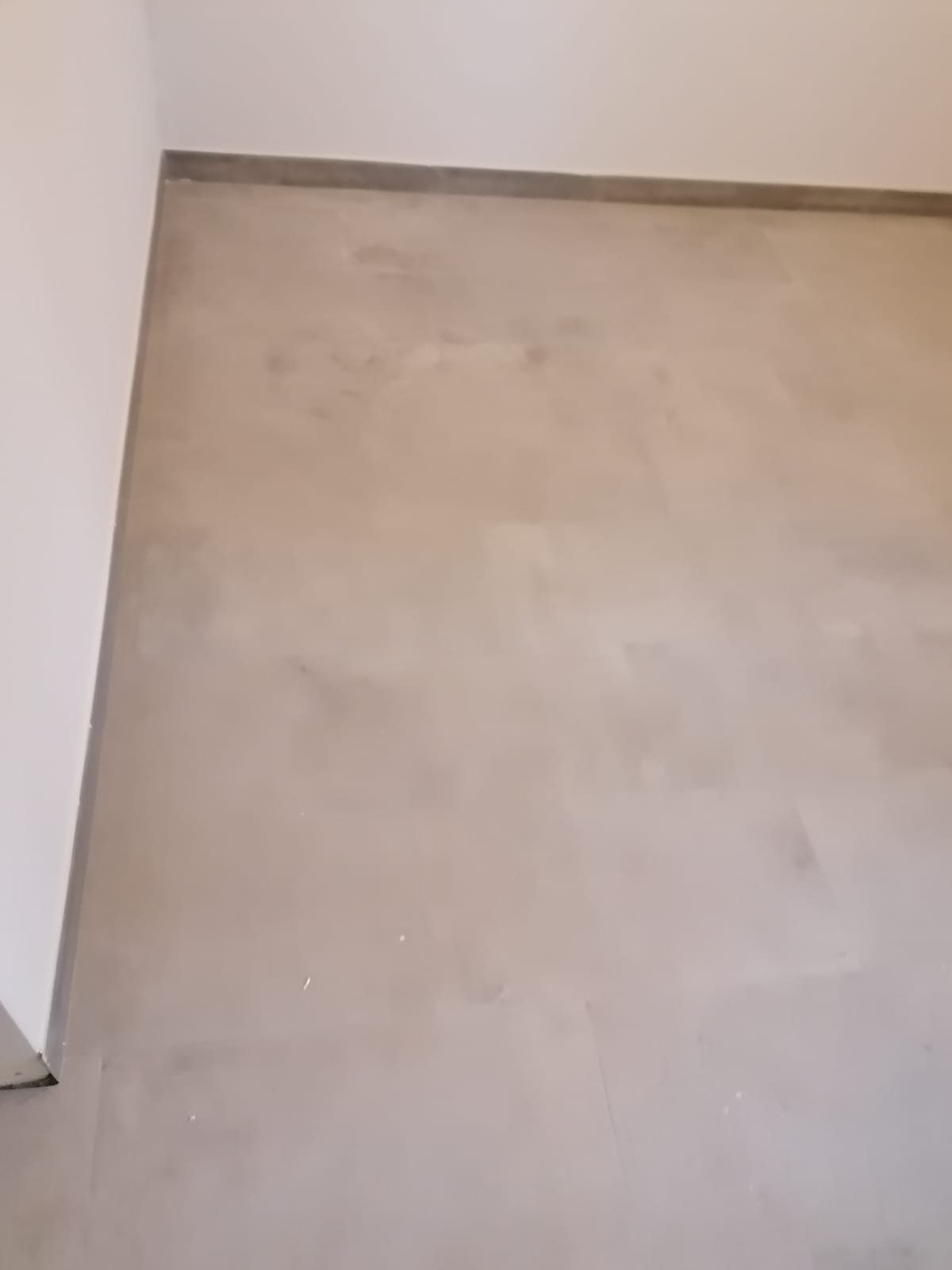 Pavimento beige grezzo con parete e battiscopa bianchi nell'angolo di una stanza
