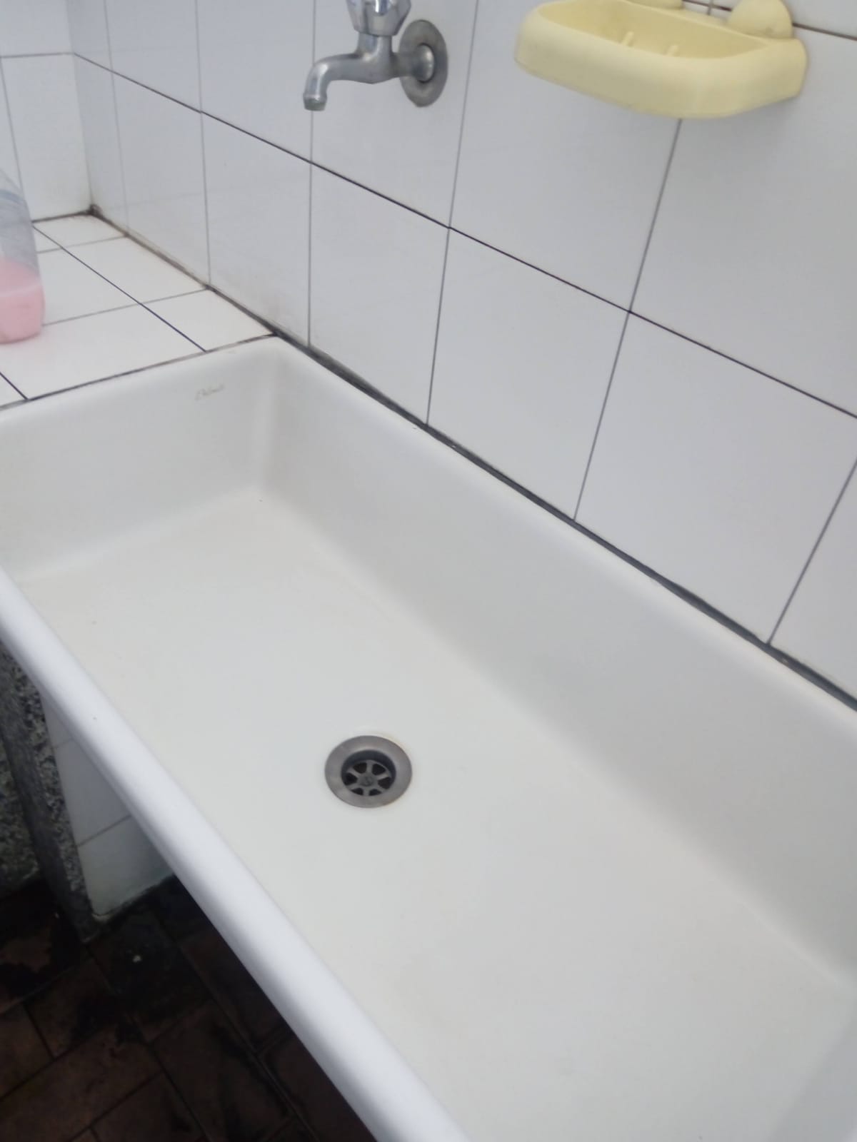 Piccola vasca da bagno bianca con pareti piastrellate, rubinetto e portasapone in un bagno.