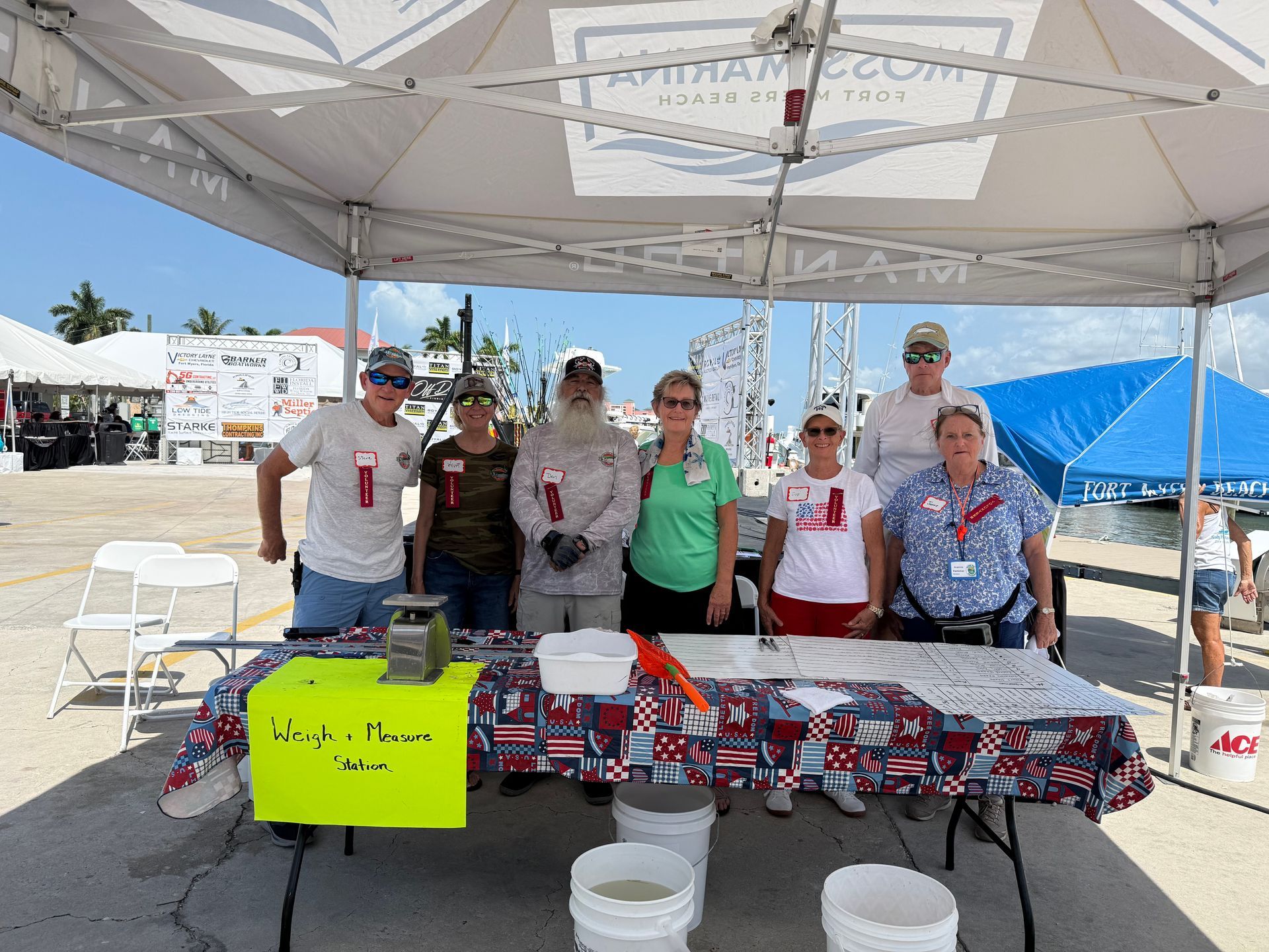 Volunteers behind a table of boxed supplies under a canopy at an outdoor event.