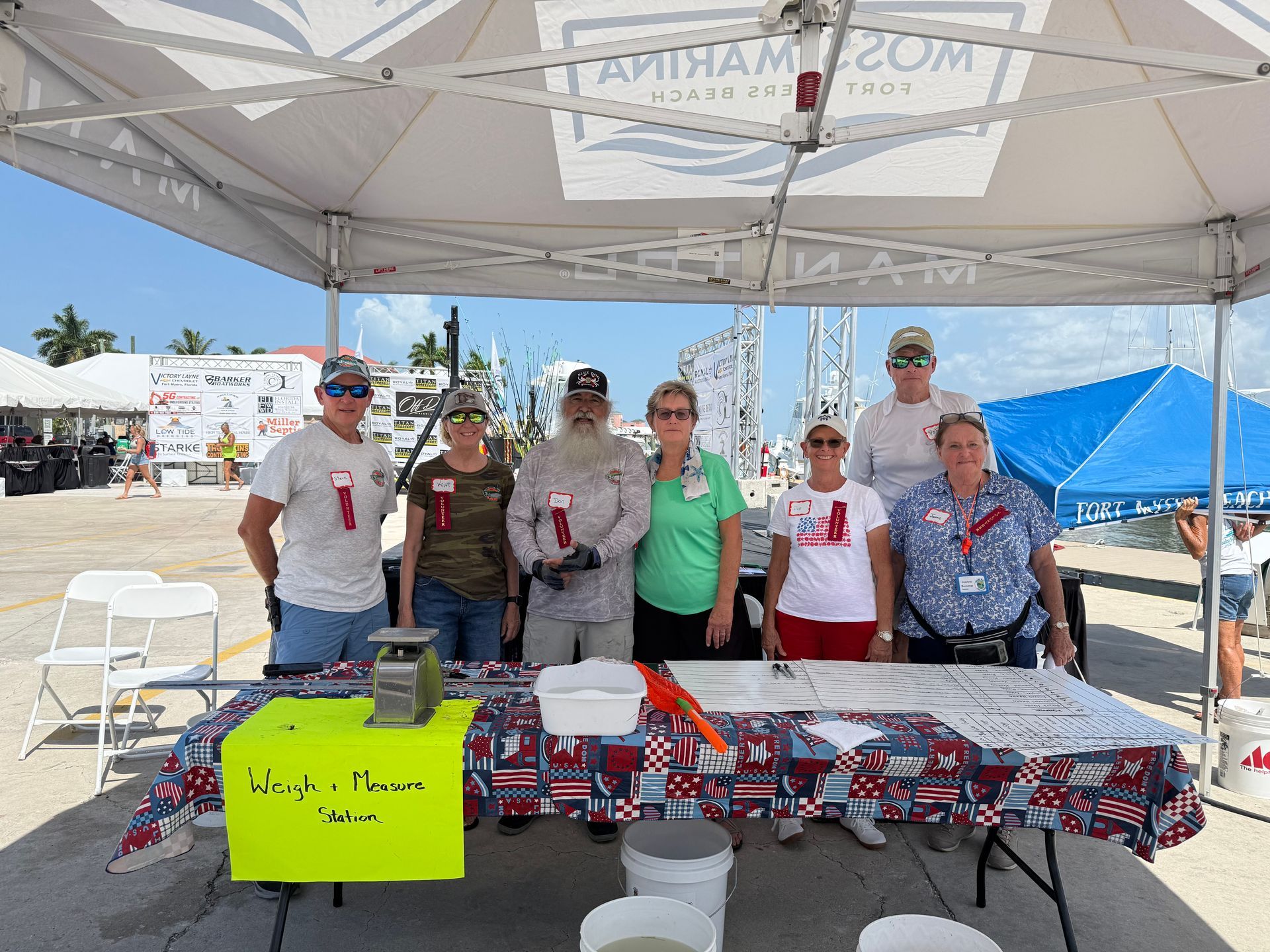 Six volunteers standing behind a decorated table under a canopy at an outdoor event