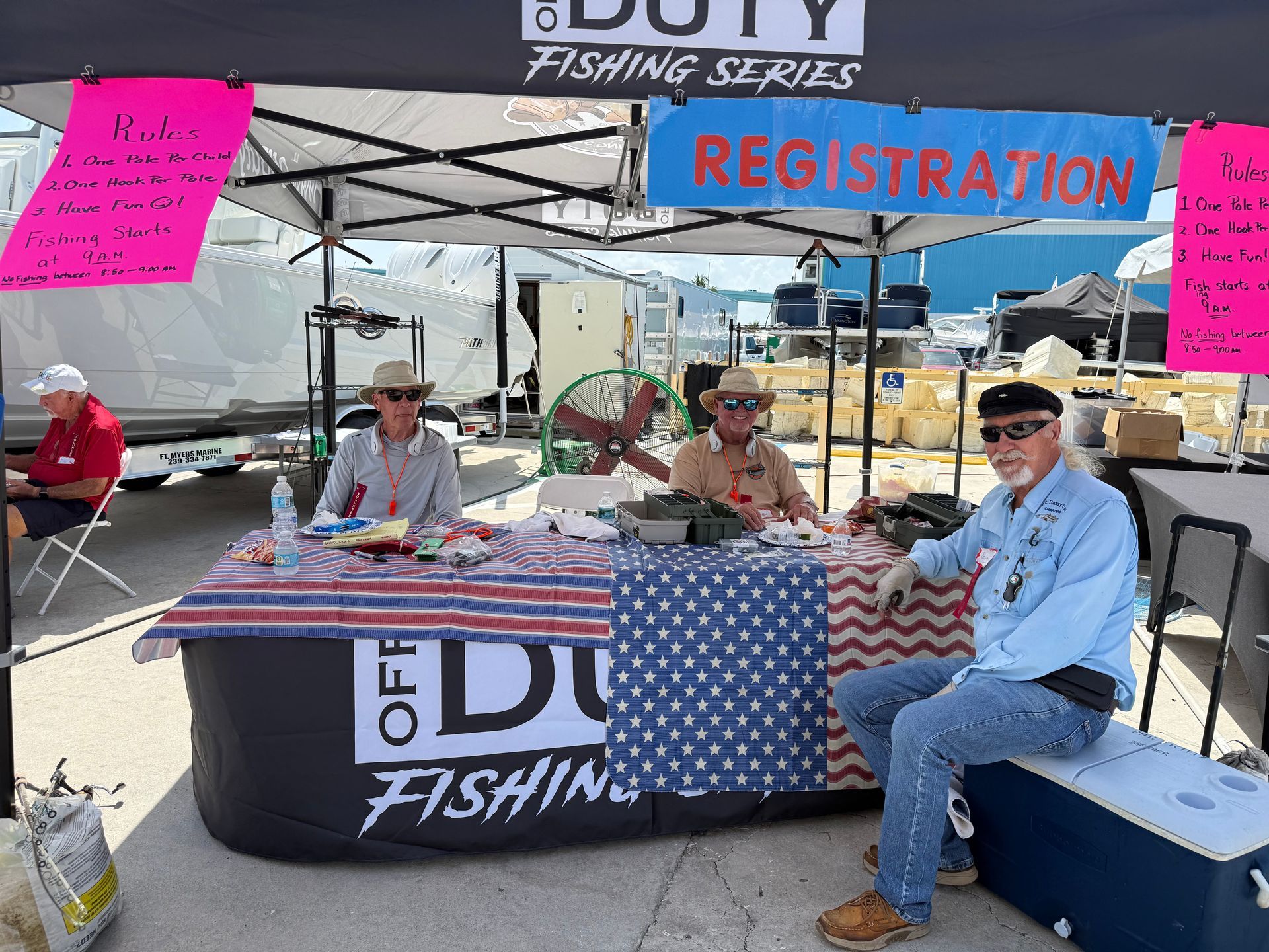 Fishing event registration booth with volunteers seated under a canopy and a red “REGISTRATION” sign.