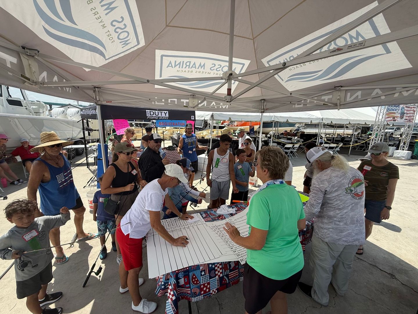 People gathered around a table under a tent, participating in a busy outdoor community event.