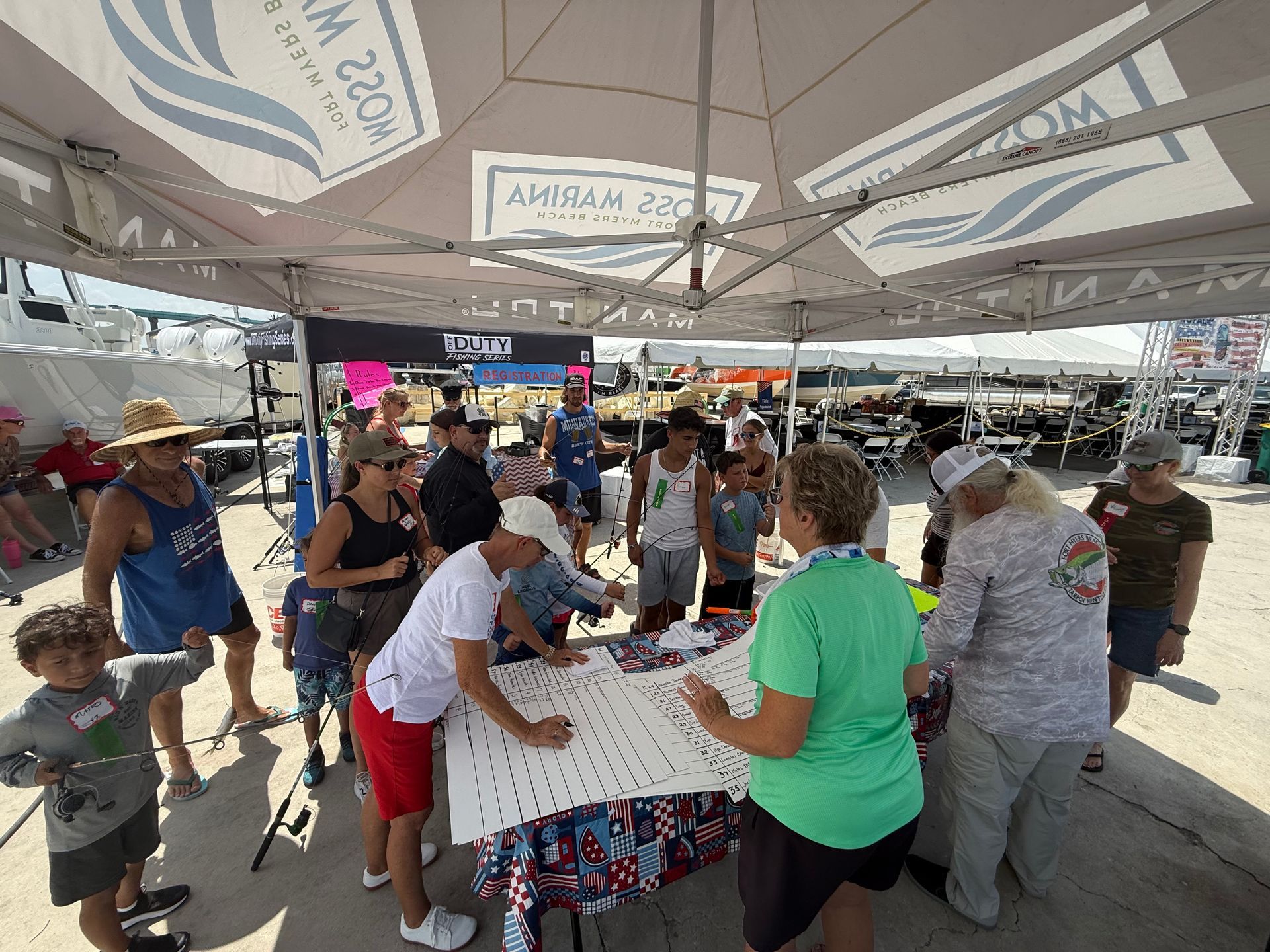 People gathered around a table under a tent, participating in a busy outdoor community event.