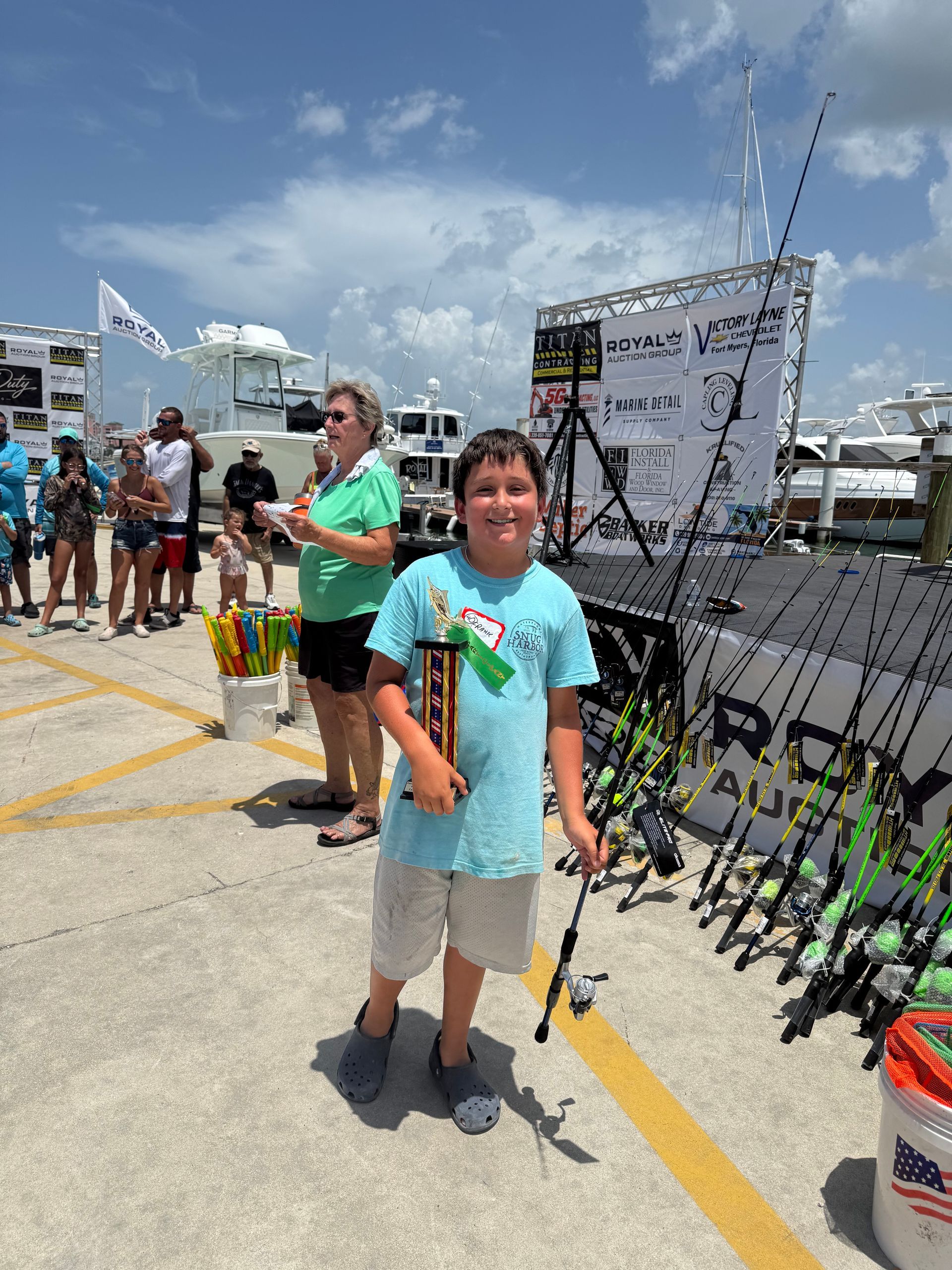 Boy standing by fishing rods at an outdoor fishing event on a sunny day