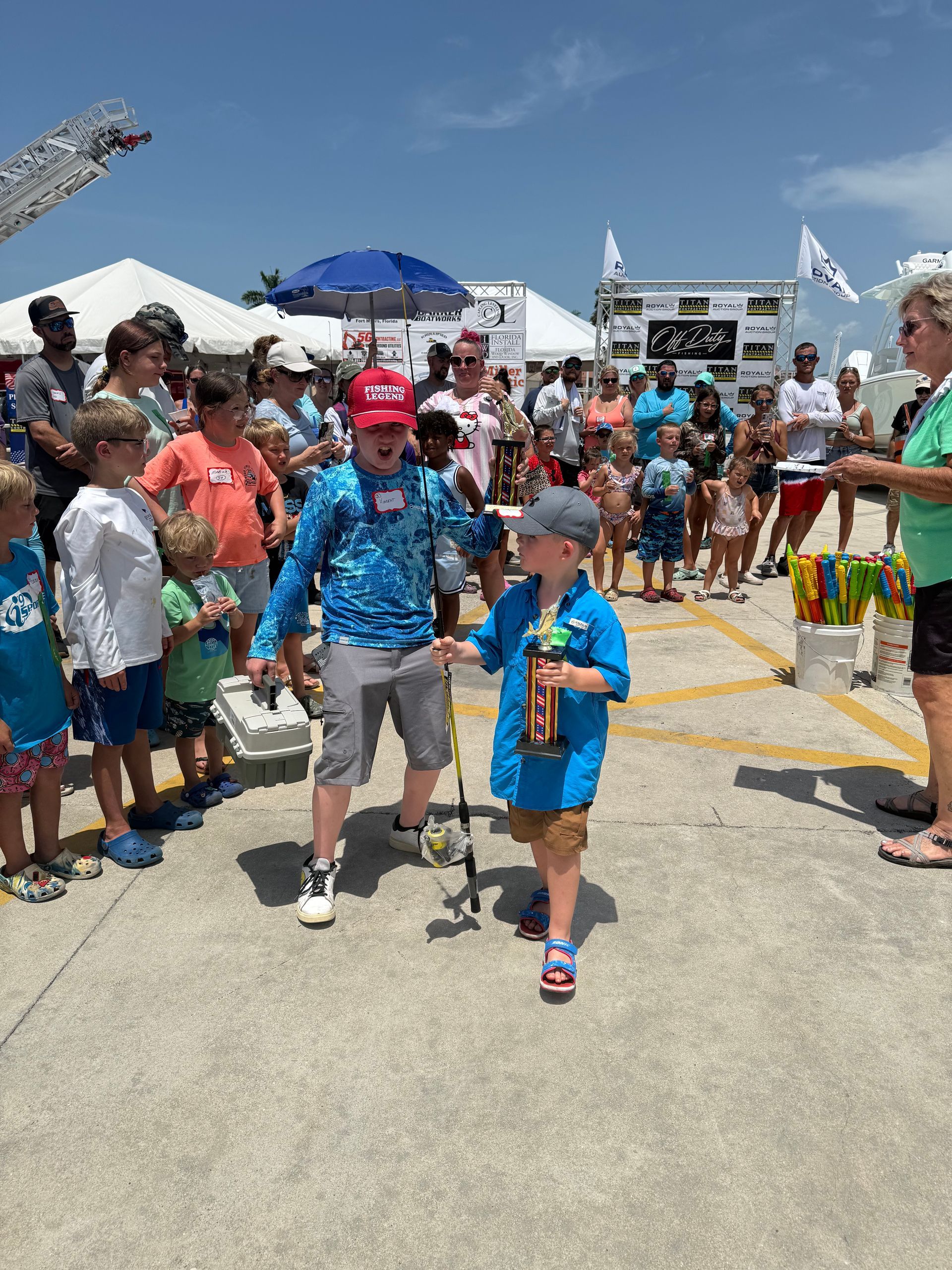 Crowded outdoor event with two children walking on a sunny street, surrounded by spectators and tents