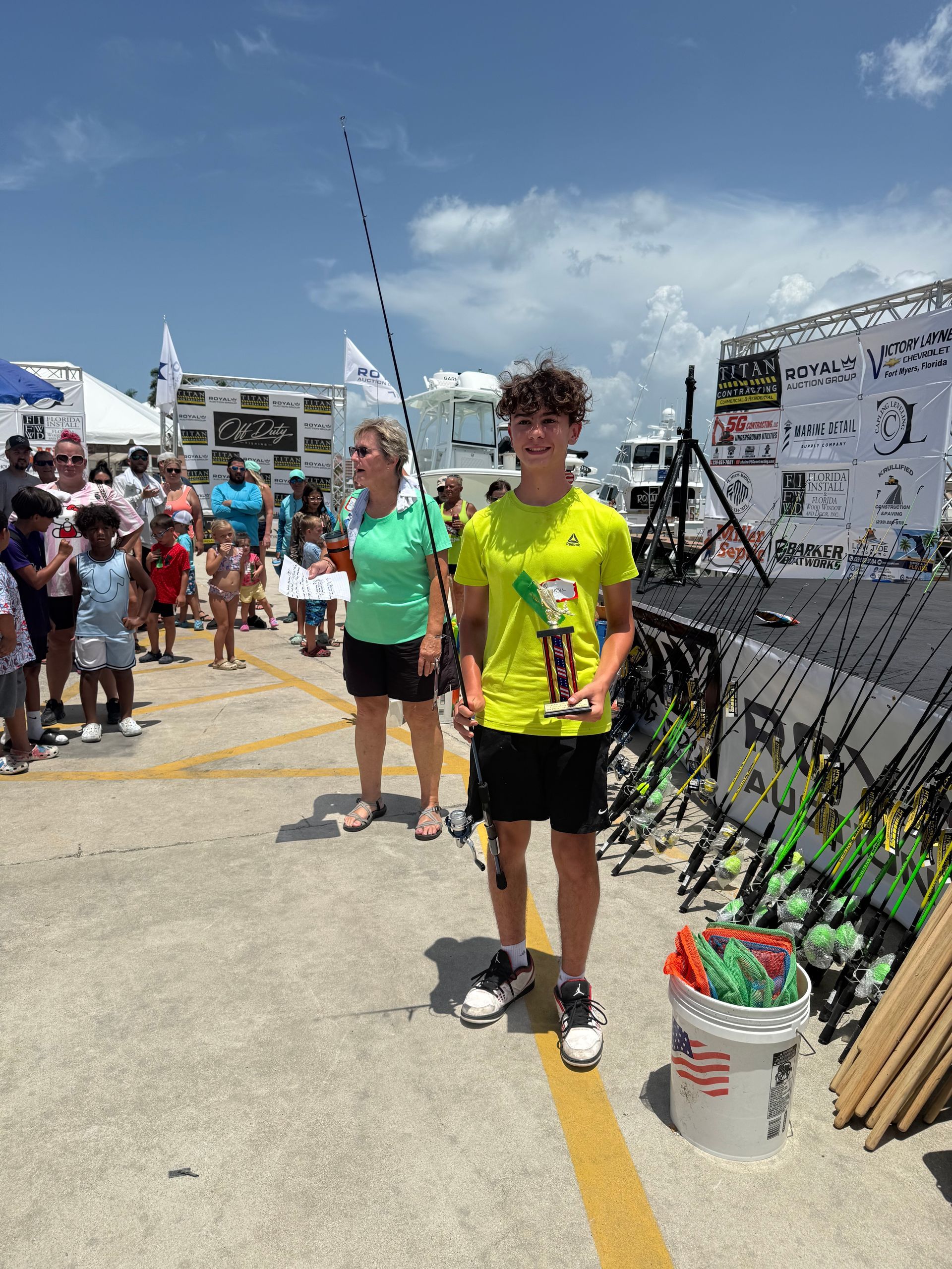 Two people standing at a sunny outdoor event beside a yellow line and display tents