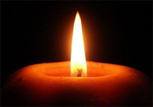 Lit candle with orange wax and a bright yellow flame against a black background.