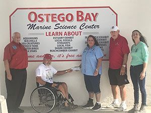 Group posing by an Ostego Bay Marine Science Center sign, including one person in a wheelchair.