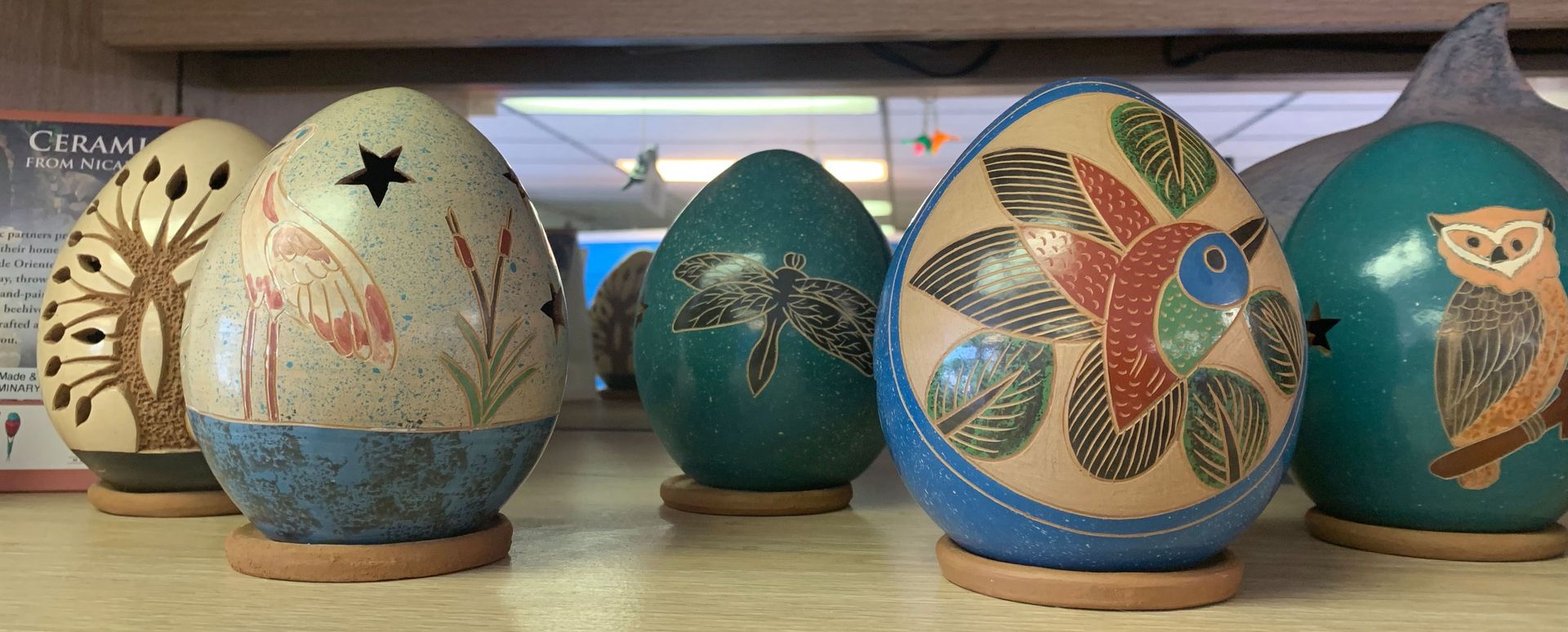 Decorative painted egg sculptures in cream, blue, and teal displayed on stands indoors