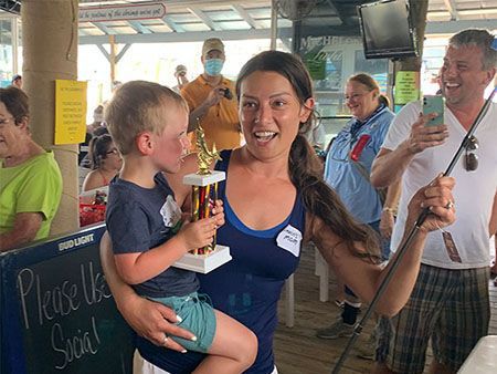 Smiling woman holding a trophy with a child on her hip at a lively indoor event