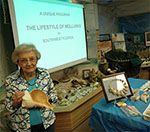 Woman holding a large shell, giving a presentation on the lifestyle of mollusks. She stands in front of a display of shells.