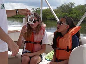 Two people wearing life jackets on a boat, one being handed a clear cup over the water