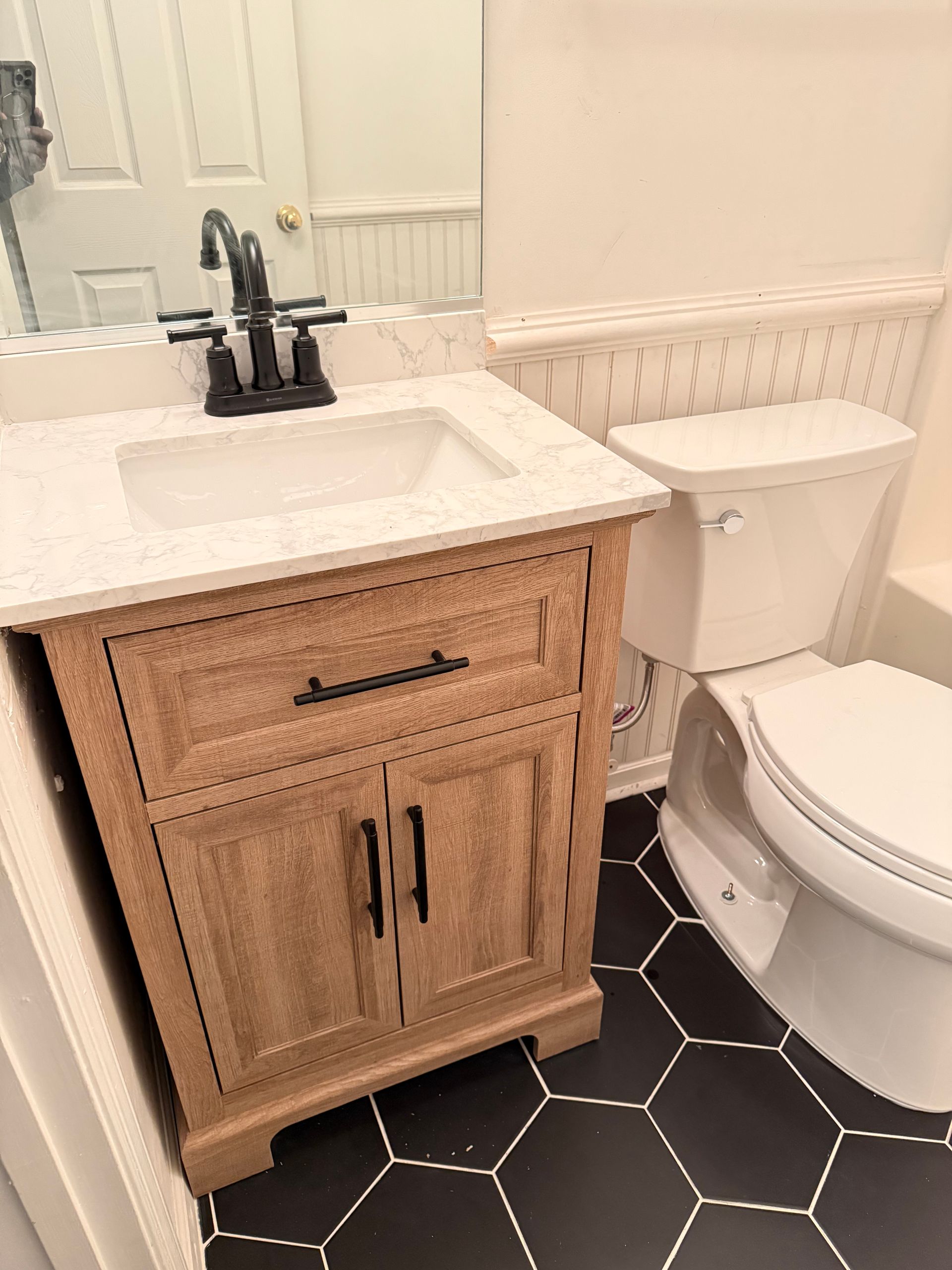 Bathroom with a light brown vanity, white countertop, and black and white hexagon tile floor.