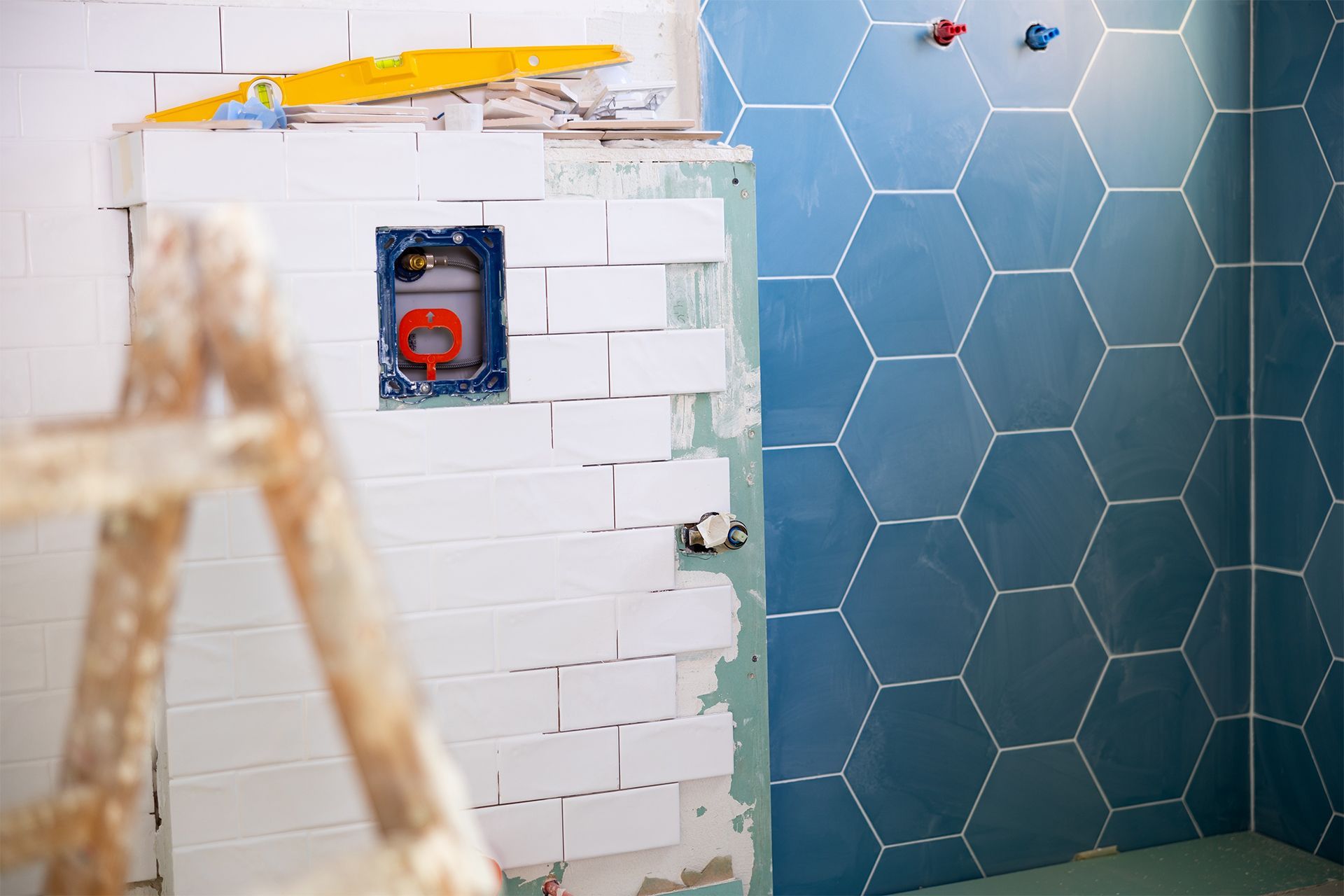 Bathroom under renovation, featuring blue hexagon tiles and white brick tiles, with ladder in foreground.