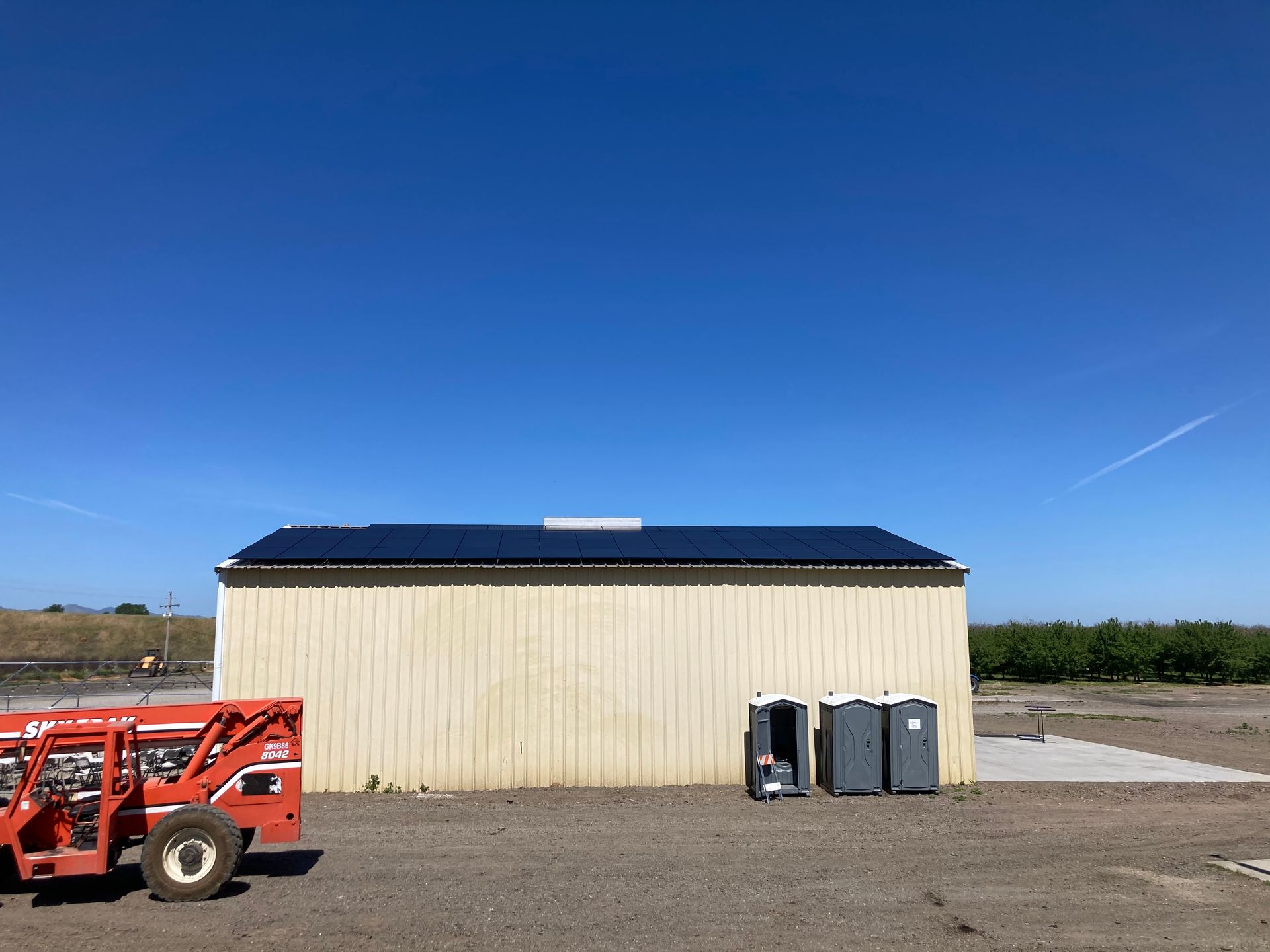 A forklift is parked in front of a building with solar panels on the roof.