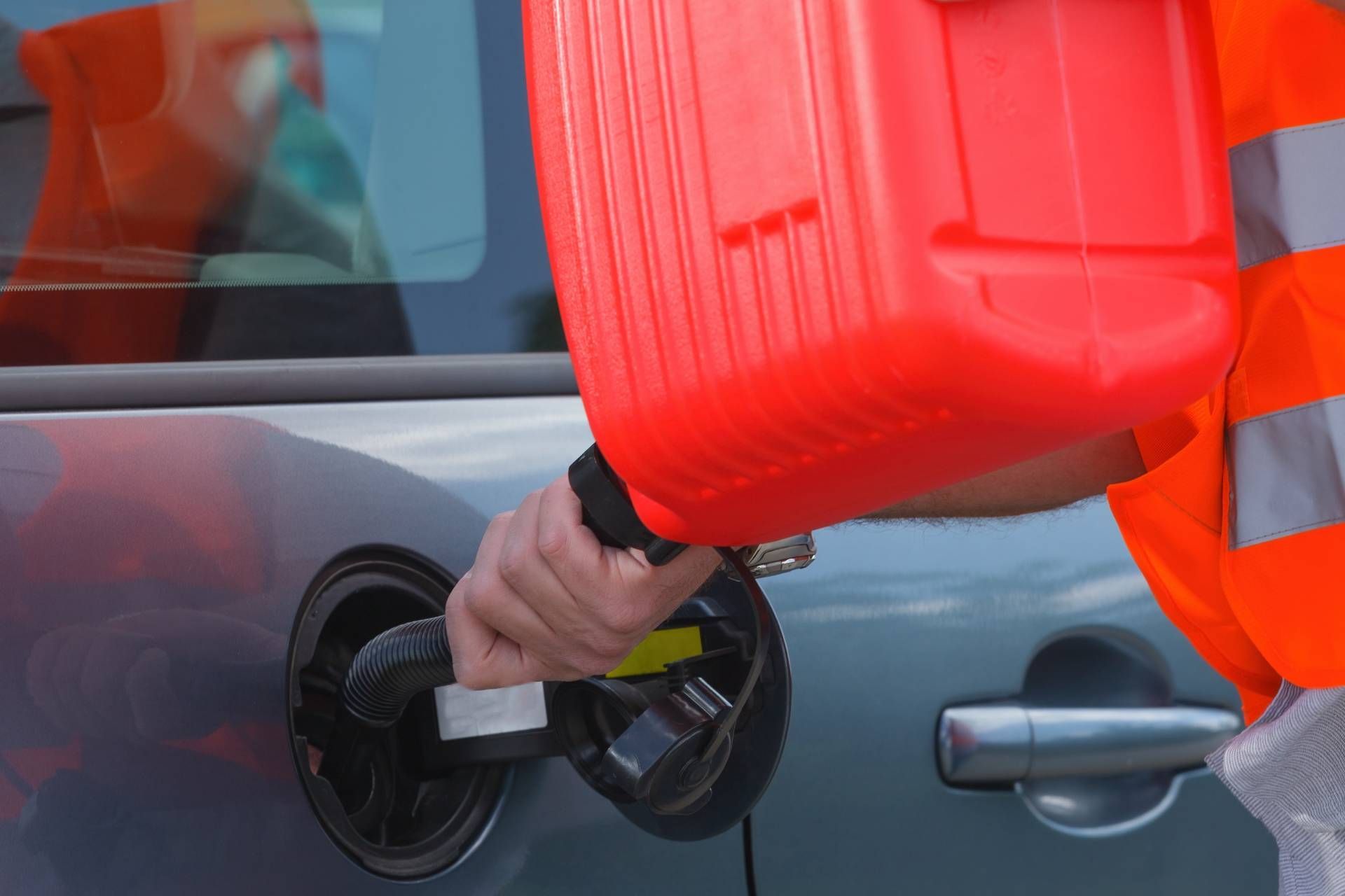 Person filling a car's gas tank from a red gasoline container; wearing an orange safety vest.