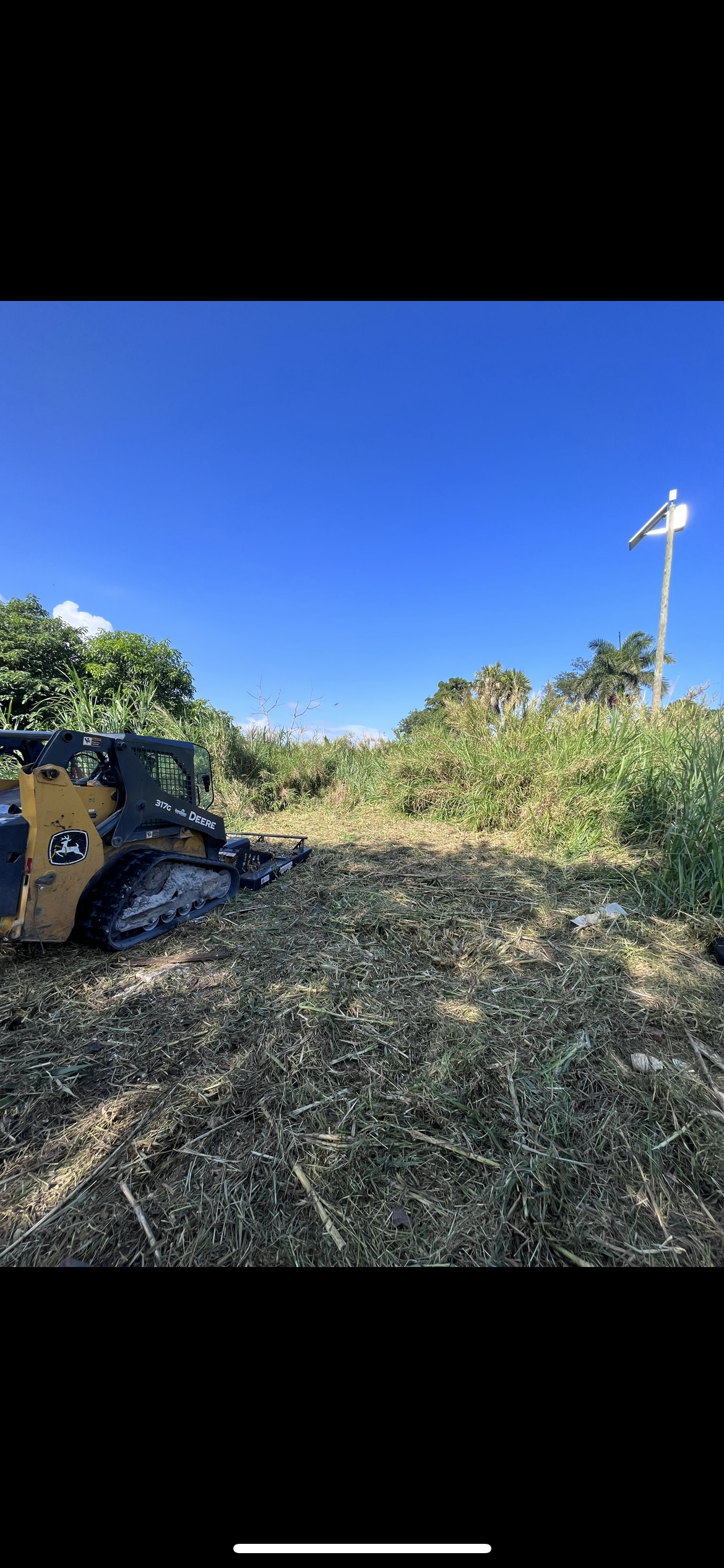 Bulldozer pushing a large pile of branches and debris in a sunny outdoor field
