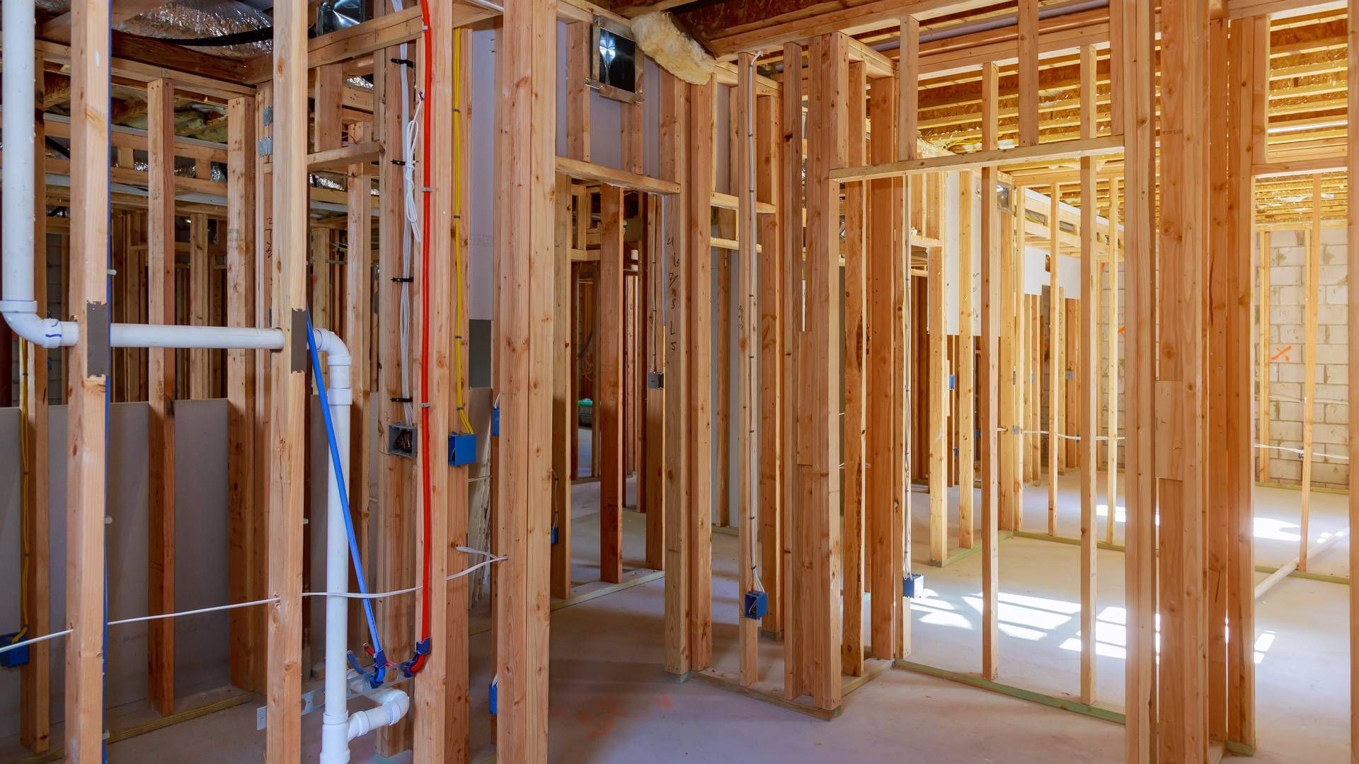 Interior view of a house under construction, showing wood framing, plumbing, and electrical work.