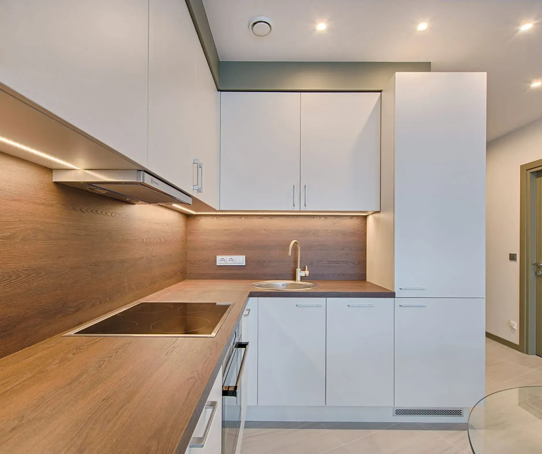Modern white kitchen with wooden countertops and backsplash, stainless steel appliances.