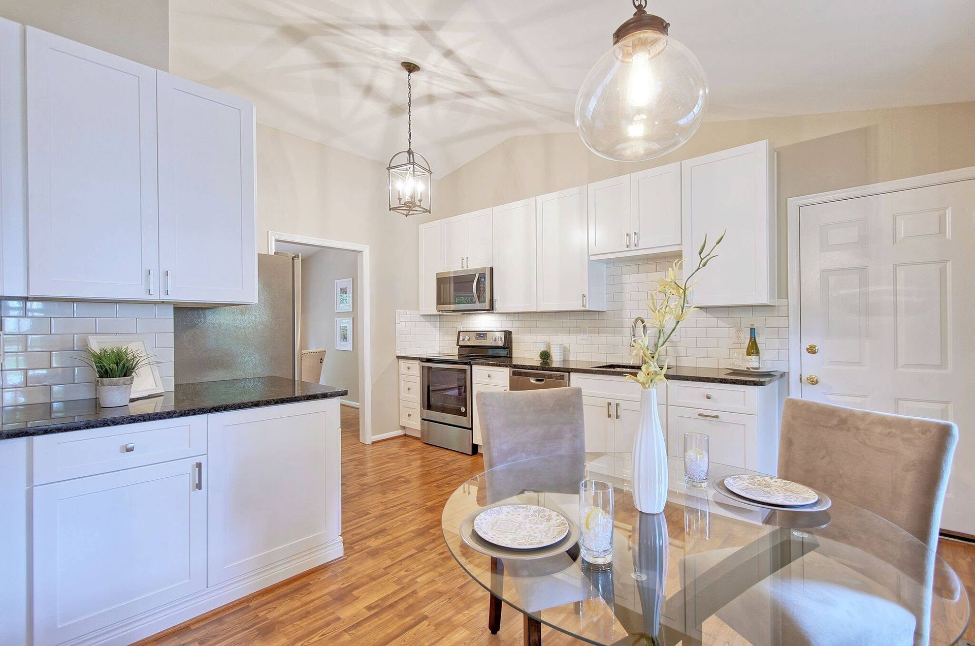 Bright modern kitchen with white cabinets, stainless appliances, glass dining table, and pendant lights