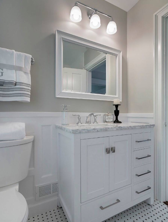 Bright white bathroom vanity with mirror, lights, sink, toilet, and marble countertop