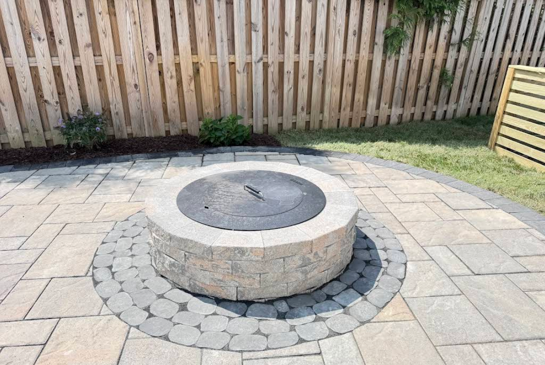 Backyard stone fire pit with circular paver patio and wooden fence