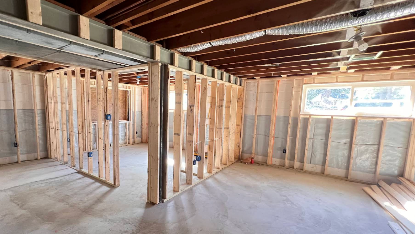 Interior of unfinished room with exposed wood framing, ceiling joists, and concrete floor, lit by a window