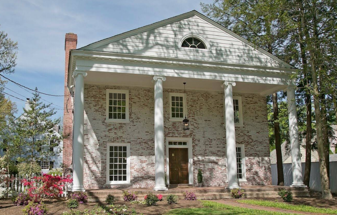 White two-story colonial house with tall columns, brick chimney, and trees in front