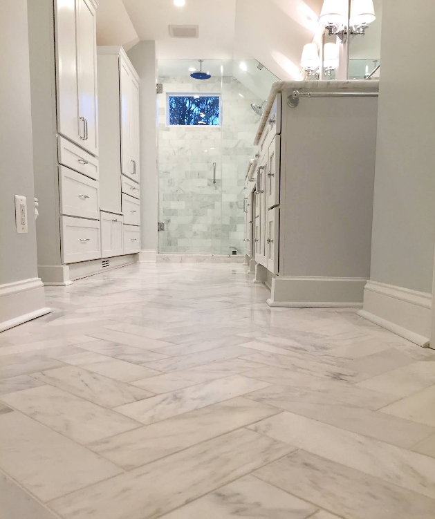 Bright white bathroom hallway with marble floor, vanity cabinets, tiled shower, and skylight.
