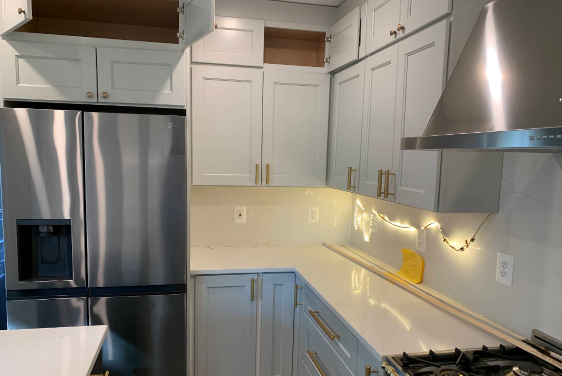 Modern white kitchen with stainless steel appliances, string lights, and light countertops